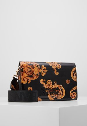 Sac bandoulière noir brillant avec motifs baroques dorés ornés et large sangle noire avec texte en relief, présenté sur un socle blanc.