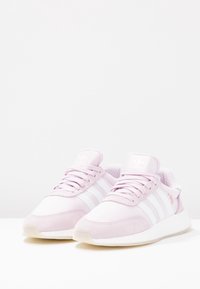 Rosa och vita sneakers med en texturerad överdel i mocka och mesh, utrustade med tre vita ränder, en vadderad sula och en stoppad krage.