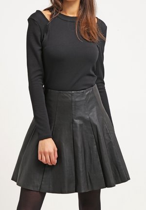 Donna che indossa un top nero a maniche lunghe con apertura sulla spalla e una gonna plissettata in pelle nera.