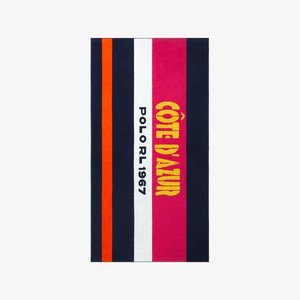 Serviette de plage ornée de larges rayures bleu marine, orange, blanche, rose et jaune avec les inscriptions "CÔTE D'AZUR" et "POLO RL 1967" bien visibles. Texture douce.