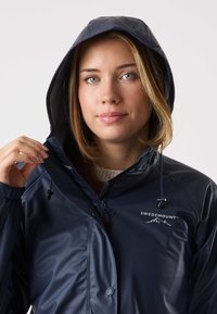 Navy waterproof jacket with a hood, featuring a front zipper, drawstring, and logo on the chest. Smooth, shiny texture, and adjustable cuffs.