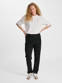 T-shirt bianco in cotone con scollatura rotonda e maniche corte. Pantaloni jogger neri con strisce laterali e vita elasticizzata. Sneakers argento.