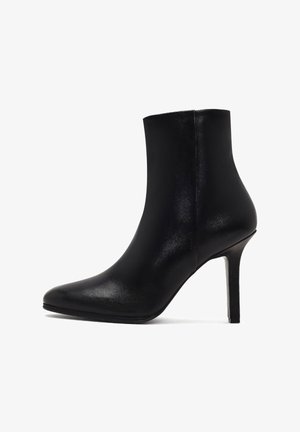 Zwarte leren enkelboot met een spitse neus, slanke hoge hak, gladde textuur en naadloos ontwerp, dat aan de bovenzijde naar boven toelopt.