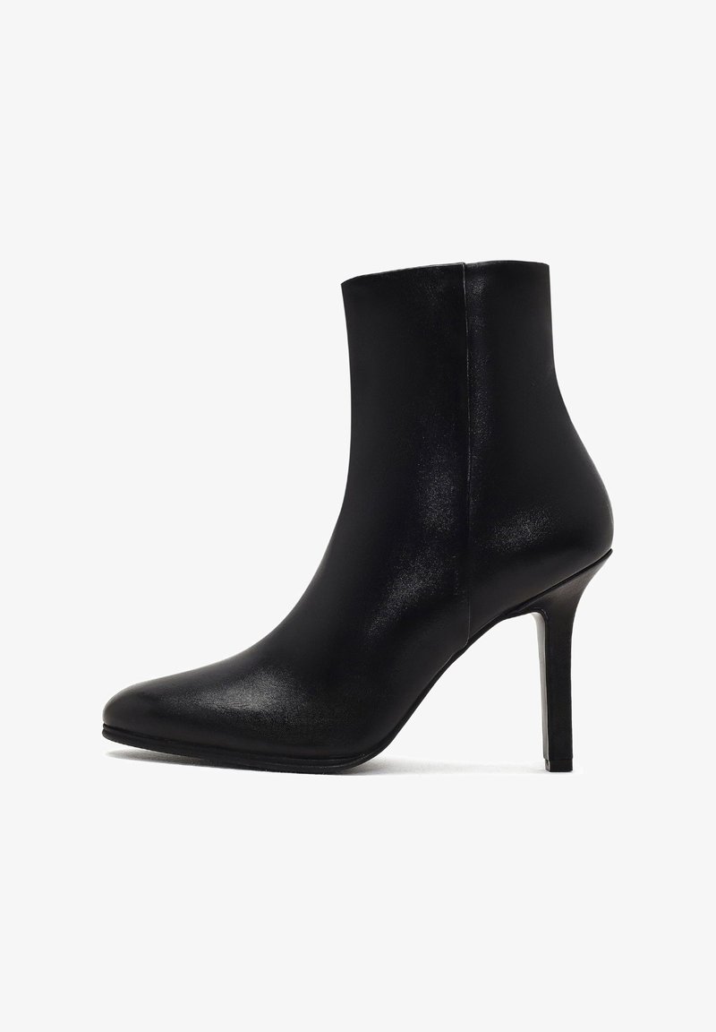 Bottine en cuir noir avec un bout pointu, un talon haut élancé, une texture lisse et un design sans couture, s'effilant vers le haut.