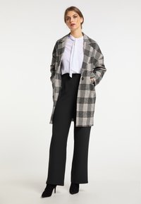 Palton în carouri gri și negru cu accente albe, având o croială relaxată, două buzunare frontale și asortat cu pantaloni negri cu talie înaltă.