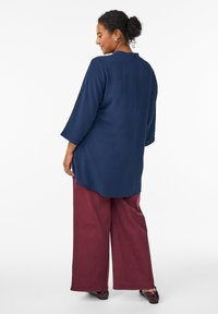Tunic blu navy con maniche a tre quarti e vestibilità rilassata, abbinata a pantaloni larghi color bordeaux. Texture liscia e design con orlo arrotondato.