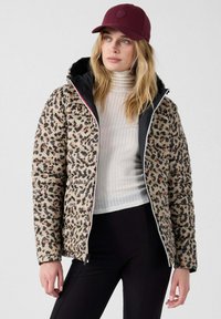 Jasje van pufferstof met luipaardprint en zwarte voering, met ritssluiting en een sportieve pasvorm. Draag het over een witte geribde coltrui en zwarte broek.