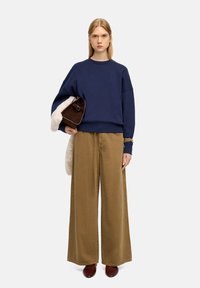 Granatowy, oversize'owy sweter, beżowe spodnie szerokie, brązowa torba z akcentem z baranka i brązowe buty. Prosty, swobodny strój.