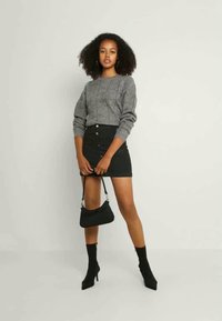 Pull en tricot gris avec un motif texturé, associé à une jupe en denim noir avec des boutons devant. Accessoirisé avec un petit sac noir.