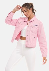 Roze denimjack met lange mouwen, knoopsluiting, twee borstzakken en versleten details. Gekocht boven een witte geribbelde top en broek.