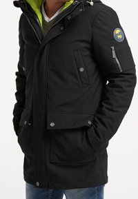 Černá bunda s matným povrchem, zelenou podšívkou, více předními kapsami a kapsou na zip na rukávu. Obsahuje velké knoflíky a logo.