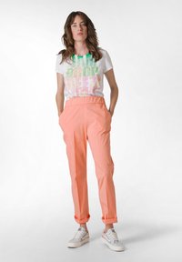 T-shirt bianca con testo colorato, abbinata a pantaloni a sigaretta corallo, dotati di cintura elastica e due tasche laterali. Sneakers bianche.