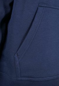 Gros plan d'une poche de sweat-shirt bleu marine avec des coutures visibles et un ourlet côtelé en bas.
