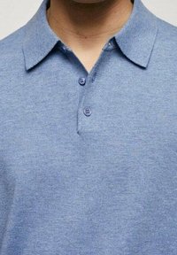 Uomo che indossa una polo azzurro chiaro con colletto e due bottoni visibili, mostrato dalla zona del collo fino a metà petto.