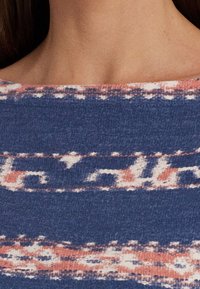 Tejido azul texturizado con un patrón sutil en coral y blanco. Presenta un escote amplio y un corte relajado, adecuado para el uso informal.