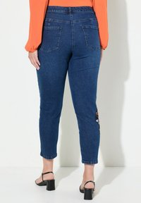 Tummansiniset farkut, joissa on istuva leikkaus ja takataskut sekä kukkakirjontaa vasemmalla lahkeella. Keskikorkea vyötärö.