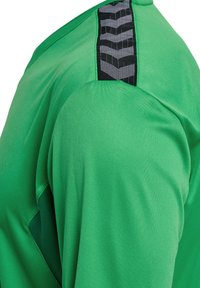 Groene sportshirt met een gestructureerde zwarte streep op de schouder. Gemaakt van een gladde, lichte stof die is ontworpen voor comfort en flexibiliteit.