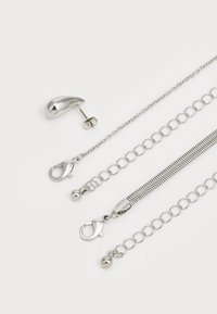 Ensemble de bijoux en argent comprenant des boucles d'oreilles à clou polies, trois styles de chaînes et divers fermoirs. Des surfaces texturées et lisses sont visibles.