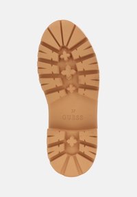 Suela de zapato de goma, color marrón claro, con patrones de textura y el nombre de la marca "GUESS" en relieve. Talla 37 marcada en la suela.