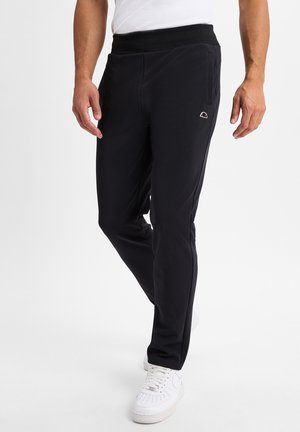 Black athletic pants with a thick elastic waistband, side pockets, and a small logo on the thigh, paired with white sneakers.