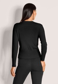 Schwarzer gestrickter Pullover mit langen Ärmeln, geripptem Saum und glatter Textur, kombiniert mit schwarzen Leggings, von hinten betrachtet.