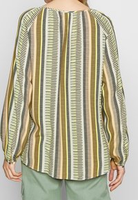 Blouse à manches longues avec un motif rayé multicolore dans des tons terreux, à coupe décontractée et avec des détails de poignet froncés.