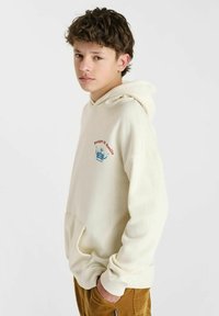 Crème kleurige hoodie met een voorzak, voorzien van rode en blauwe grafische tekst en ontwerp. Zachte textuur, relaxte pasvorm en verstelbare capuchon.