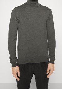 Grauer Rollkragenpullover aus Strickstoff, mit langen Ärmeln und slim Fit, kombiniert mit dunklen Cordhosen.