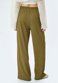 Pantaloni a gamba larga verde oliva realizzati in tessuto texture con vita elastica. Presentano una vestibilità rilassata e una silhouette fluida.