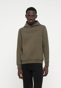 Sweat à capuche vert olive en mélange de coton doux. Doté d'une poche kangourou et d'un imprimé de logo sur la poitrine. Finitions avec des poignets et un ourlet côtelés.