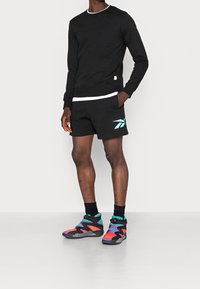 Czarna bluza z okrągłym dekoltem, połączona z czarnymi szortami z turkusowym logo. Kolorowe sportowe buty za kostkę o teksturowanej powierzchni.