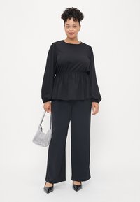 Black long-sleeve top with a peplum waist, paired with loose black pants, a checkered handbag, and pointed studded heels.