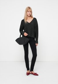 Maglione corto nero e testurizzato; jeans skinny neri; ballerine rosse; borsa a mano nera e angolare; sfondo chiaro. Stile minimalista.