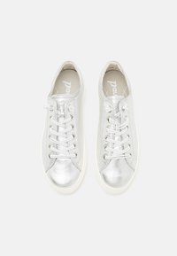 Sølv sneakers med metallisk finish, rund tå og hvit gummisåle. Snøre er vevd gjennom sølvfargede øyer. Teksturen er glatt.