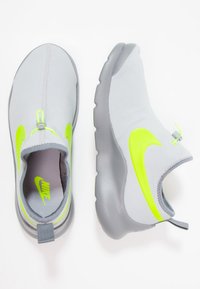 Pair of light grey slip-on Nike sneakers with neon yellow swoosh logo and gray soles, one viewed from above and the other from the side.