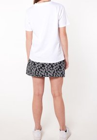 Bílé tričko s krátkým rukávem v kombinaci s černou mini sukní s bílým květinovým vzorem. Oblečení doplňují bílé tenisky.
