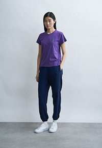 Μωβ κοντομάνικο μπλουζάκι με πράσινο λογότυπο, συνδυασμένο με ναυτικό μπλε τζόγκερ. Και τα δύο ρούχα έχουν άνετη εφαρμογή και ομαλή υφή.