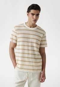 Beige en witte gestreepte korte mouwen gebreide t-shirt met een ronde hals en een gestructureerde stof. Zit losjes op het lichaam.