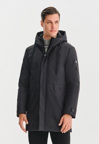 Czarna kurtka parka z kapturem, wykonana z gładkiego, wodoodpornego materiału. Posiada przednie kieszenie oraz dyskretną logo na rękawie. Regulowane troczki w kapturze.