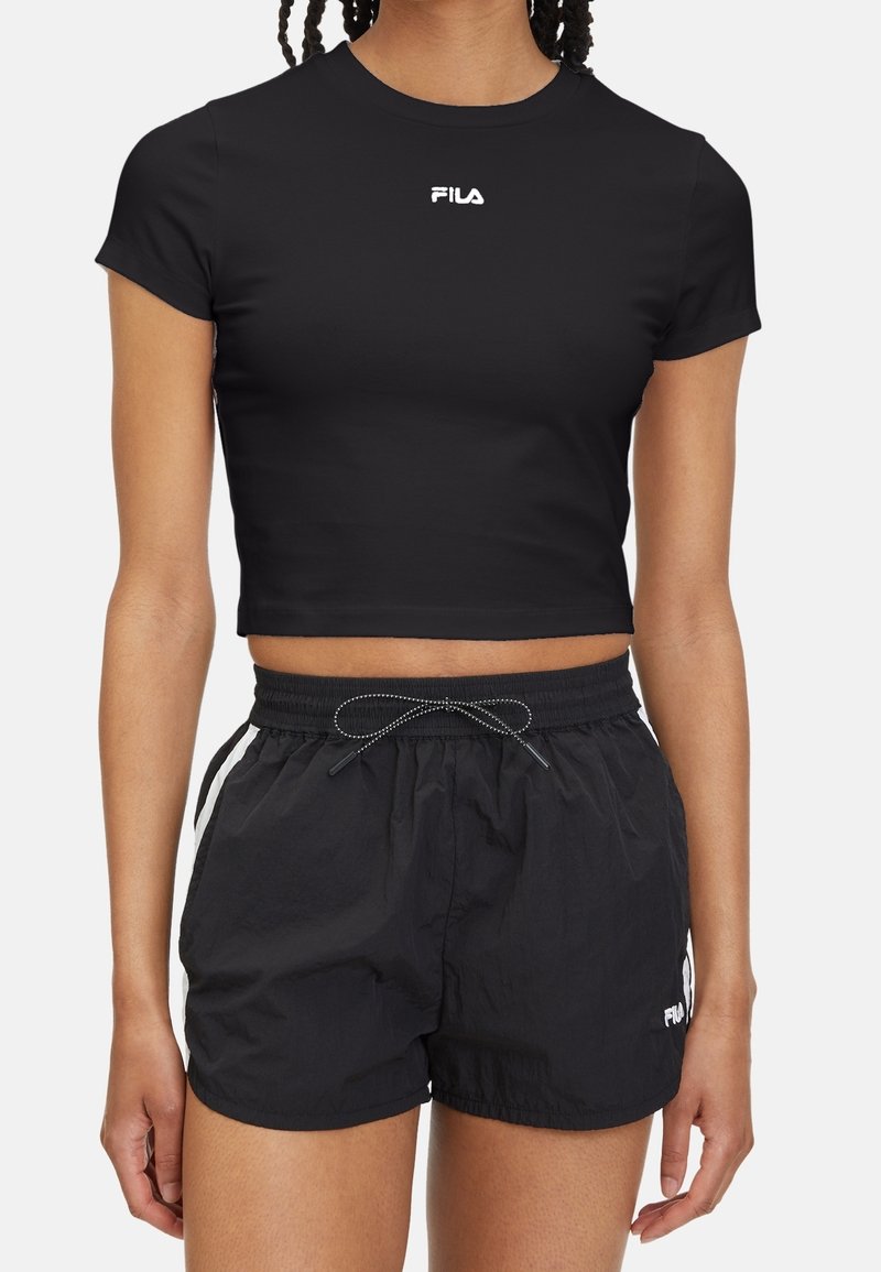 Femme portant un t-shirt court noir FILA et un short noir à cordon avec un logo blanc sur la cuisse gauche.
