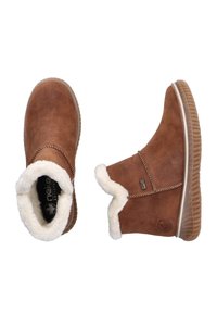 Bottes chelsea en suede marron avec doublure en fausse fourrure blanche, semelle en caoutchouc texturé et couture décorative sur le dessus. Présente une étiquette de logo sur le côté.