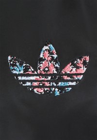 Černá látka s vyšívaným logem Adidas trefoil, které má květinový vzor v růžové, modré, bílé a černé nitě.