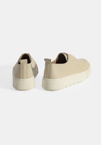 Beige instappers met een gladleren bovenwerk, ronde neus en verhoogde rubberen zool. Voorzien van een trekband aan de achterkant voor gemakkelijk aan- en uittrekken.