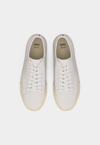 Paar weiße BOSS-Sneaker mit Schnürung, beigen Sohlen und Ortholite-Einlegesohlen, von oben auf weißem Hintergrund betrachtet.