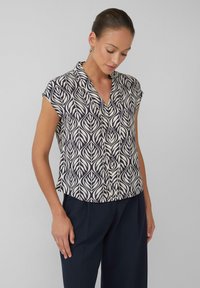 Blouse à manches courtes avec un motif de feuilles marine et crème, dotée d'un col en V et d'un ourlet légèrement arrondi, faite en tissu léger.