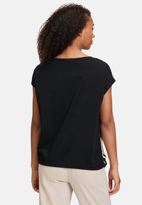 Black short-sleeve t-shirt with a loose fit, rounded neckline, and a smooth texture, worn with light-colored pants.
