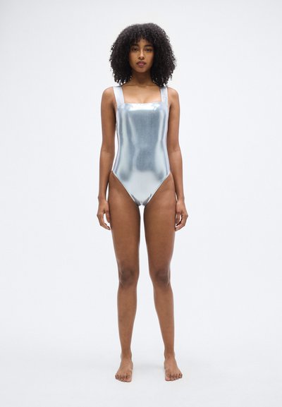 Ασημί μεταλλικό ολόσωμο μαγιό με τετράγωνη λαιμόκοψη και φαρδιές τιράντες, με λεία υφή και ψηλή κοπή στα ανοίγματα των ποδιών.