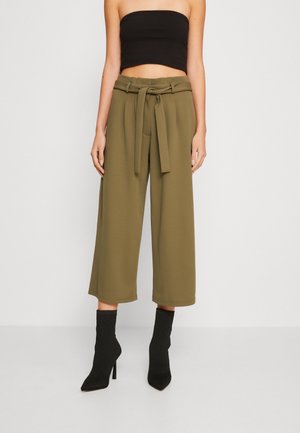 Pantalons larges verts olive avec une taille ceinturée, en tissu lisse et d'une longueur raccourcie, associés à des bottines noires texturées.