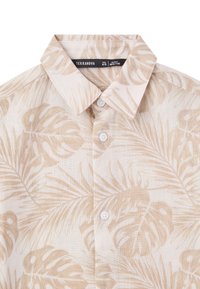 Camicia a maniche corte di un beige chiaro con motivo a foglie di palma, dotata di un colletto e bottoni bianchi per la chiusura. Realizzata in un tessuto morbido e traspirante.
