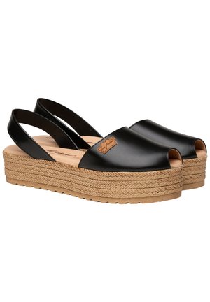 Zapatos de piel negra de punta abierta con talón de yute trenzado. Presentan un acabado suave y un pequeño logotipo en la parte superior.